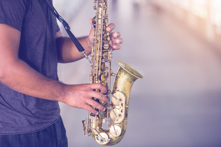 A street musician plays the saxophone with blurry people walking on skywalk in city.の写真素材