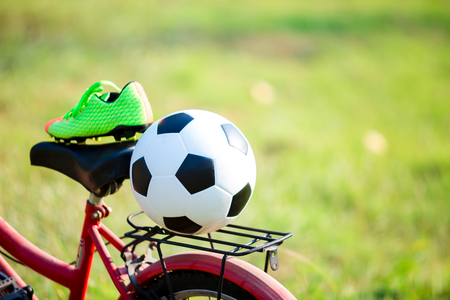 football and soccer shoes with blurry of red bicycle and green grass for outdoor sportの写真素材