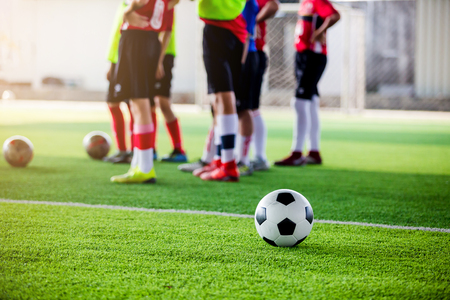 soccer ball on green artificial turf with blurry soccer players standing before training and start game.の写真素材