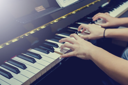 blurry fingers of young woman and a boy pressing key to play the piano with music notation. Four...