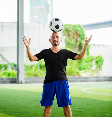 portrait of a male football player juggling a ball on his head on green artificial turfの写真素材