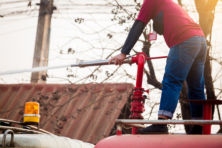 staff standing on water truck with holding fire fighting nozzle and hose with spray water to cleaning the roadの写真素材