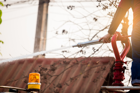 staff standing on water truck with holding fire fighting nozzle and hose with spray water to...