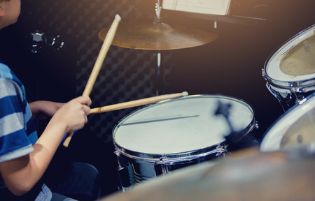blurry image of wooden drumsticks in hands of Asian kid wearing blue striped t-shirts to learning and play drum set in music room, the concept of musical instrumentの写真素材
