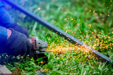 hands of worker grinding or cutting metal with grinder at outdoor lawn or construction site, with selective focus. close up shot. a lot of sparks while grinding ironの写真素材
