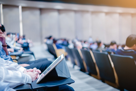 Blurry of auditorium for shareholders' meeting or seminar event, many business people play tablet and smartphone on the conference for meeting informationの写真素材