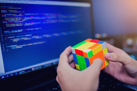 BANGKOK, THAILAND - MAY 15, 2019: Programmer holding Rubik's cube. Software developer with software coding background on laptop. solving problem and brain training concept.のeditorial素材