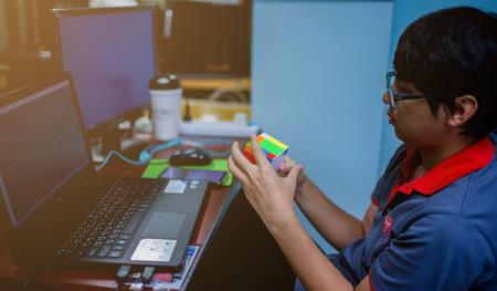 BANGKOK, THAILAND - MAY 15, 2019: Programmer holding Rubik's cube. Software developer with software coding background on laptop. solving problem and brain training concept.のeditorial素材