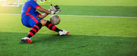 selective focus to goalkeeper is jumping to catching the soccer ball. Ball in hand of goalkeeper on artificial turf. Asian boy soccer player.の写真素材