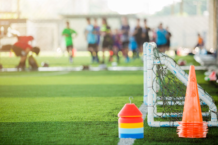 multi color of marker cones and mini goal on green artificial turf for soccer training equipment with blurry soccer team training in soccer academy.のeditorial素材