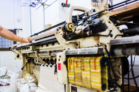 The technician's hand working with textile factory in spinning production line and a rotating machinery and equipment production company. Elastic weaving workshop. Close up and selective focus.の写真素材