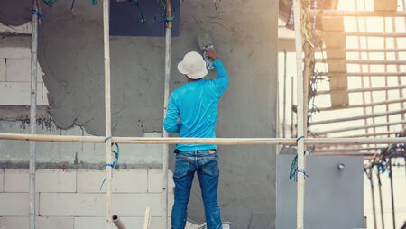 plasterer in blue working uniform plastering the wall of house building site. hands plasterer tools....