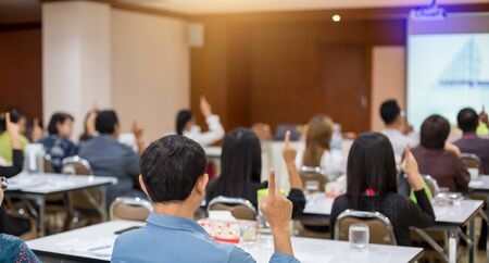 blurry image. pointing up finger with raised hands and arms of large group of people in meeting room or class room, audience voting in professional education surrounding, gesturing up with fingers.の写真素材