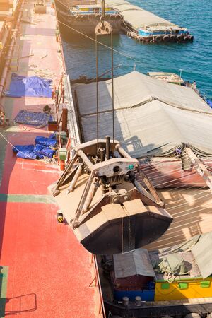 Loading wheat on cargo ship with crane and bucket. Shipment from a merchant ship to a small ship....