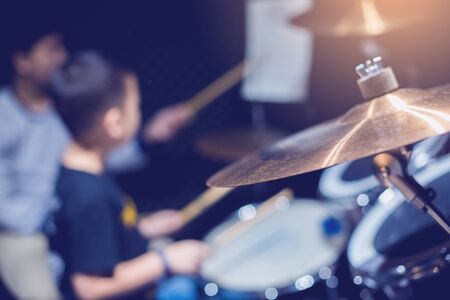 Selective focus to cymbals of drum set with blurry kid learning and play drum set with teacher in music room. The concept of musical instrument.の写真素材