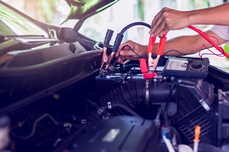 Auto mechanic use voltmeter to check voltage level in car battery. Auto mechanic working in garage. Repair service. Selective focus.の写真素材