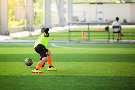 selective focus to goalkeeper is jumping to catching the soccer ball. Blurry ball after going out from hands of goalkeeper on artificial turf. Asian boy soccer player. Soccer training in academy.の写真素材