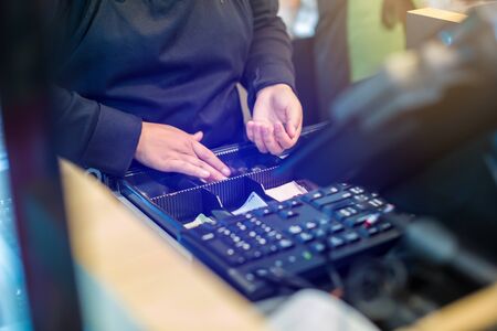 The cashier is picking up banknotes and coins inside the cash register machine. Cashier staff receive and change money to customers in the store.の写真素材