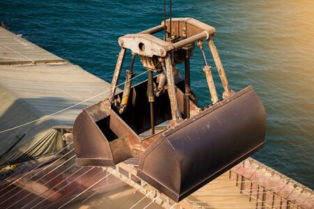 Loading wheat on cargo ship with crane and bucket. Shipment from a merchant ship to a small ship....