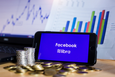 BANGKOK, THAILAND, JULY 23, 2019 : Facebook and Libra text display on smartphone with gold silver coin ,laptop and chart graph  background. The concept of business information on technology.のeditorial素材