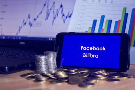 BANGKOK, THAILAND, JULY 23, 2019 : Facebook and Libra text display on smartphone with gold silver coin ,laptop and chart graph  background. The concept of business information on technology.のeditorial素材