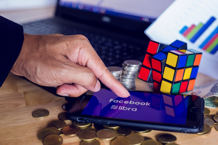 BANGKOK, THAILAND, JULY 23, 2019 : Facebook and Libra text display on smartphone with gold silver coin ,laptop, Rubik and chart graph  background. The concept of business information on technology.のeditorial素材