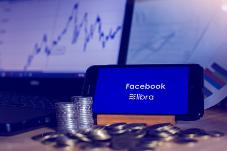 BANGKOK, THAILAND, JULY 23, 2019 : Facebook and Libra text display on smartphone with gold silver coin ,laptop and chart graph  background. The concept of business information on technology.のeditorial素材