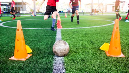 Soccer ball and marker cone with training equipment on green artificial turf with blurry player training background. Soccer Academy.の写真素材