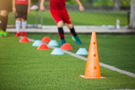 Orange marker cones on green artificial turf with blurry kid soccer player jogging between marker cones for training. Soccer training equipment.  Football or soccer academy.の写真素材