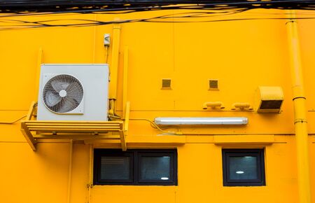 Modern air conditioner on a yellow wall. Air conditioning compressor with black glass windows on the yellow wall building background.の写真素材