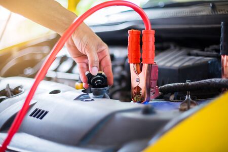 Hands of mechanic check water in car radiator and charging car battery with electricity through...