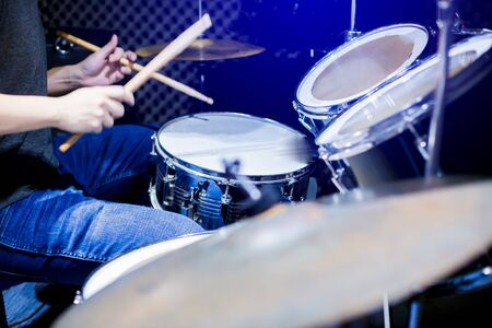 Young musicians wear t-shirts, jeans, and play the drum set and cymbals with wooden drumsticks in...