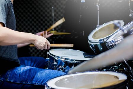Young musicians wear t-shirts, jeans, and play the drum set and cymbals with wooden drumsticks in music room , the concept of musical instrument.の写真素材