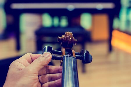 Hand tuning violin with blurry piano in music room or stage. music instrument concept.の写真素材