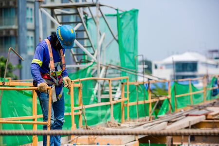 Builder worker in safety protective equipment. Professional industrial climber in helmet and uniform works at height. Risky extreme job. Industrial climbing at construction site.の写真素材