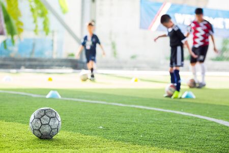 Soccer ball on green artificial turf with blurry soccer team training. Blurry kid player training and soccer equipment in soccer academy.の写真素材