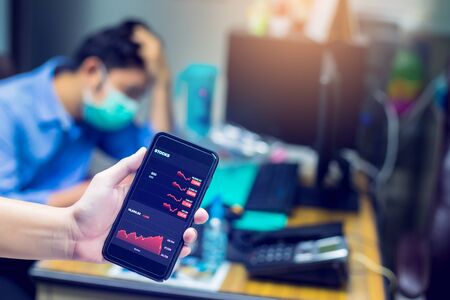 Red graph on smartphone with blurry the patient is wearing a mask. The concepts of the economic downturn from Covid 19.の写真素材