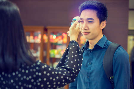 Staff check fever by digital thermometer visitor at Information counter for scan and protect from Coronavirus (COVID-19). Screening point for people before entering the building.のeditorial素材