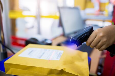 Selective focus to barcode reader in hand of staff in post office. Parcel on the digital scale to calculate the shipping cost from the weight in post office.の写真素材