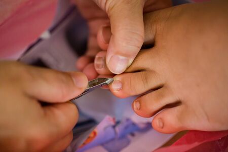 Selective focus to woman cutting nails to a hygiene child. Female hands hold nail scissors and child's foot. Manicure for kid by hand of scissor to cut nail for clean.の写真素材