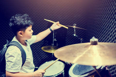 Asian boy put white t-shirt learning and play drum set with wooden drumsticks in music room, the concept of musical instrumentのeditorial素材