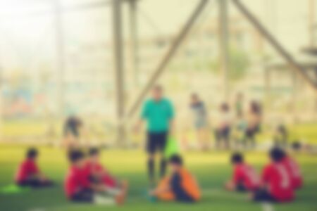 Blurry young boy soccer players sitting with coach on green artificial turf. Blurry sport background.の写真素材