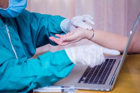 The doctor wears gloves and a medical mask to checking patience's pulse. Medical checking on in hospital. Asian doctors prevent Coronavirus Covid-19 infection while treating patients.の写真素材