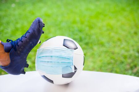Mask wearing to football with foot and sport shoe of soccer player. The concept of Covid-19 impact  to  football matches.の写真素材