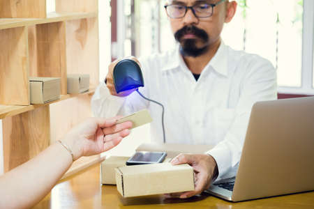 Asian staff working to using barcode reader to scan customer smartcard for read information in post office. He is bald to working with barcode reader, smartphone, laptop and customer smart card.の写真素材