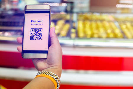 Selective focus to QR Code tag on smart phone in hand of customer with blurry gold jewelry shop to accepted generate digital pay without money. Qr code payment concept.の写真素材
