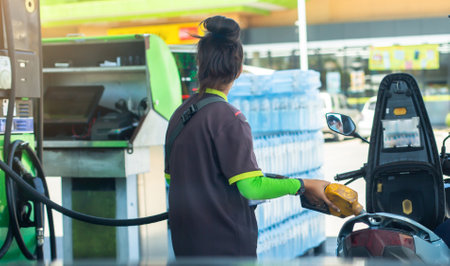 Woman staff hold yellow fuel nozzle to refilling the motorcycle in the gas  station, Refilling the...