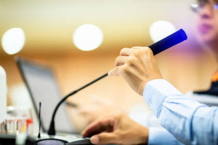 Selective focus to hand and desktop wireless conference microphones with blurry businessman wearing mask in a meeting room, microphone on the desk in meeting room with blurry speaker.の写真素材