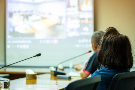 Selective focus to business woman with blurry business man speaking to desktop conference microphones and projector  in a meeting room. Background of business meeting and presentation.の写真素材