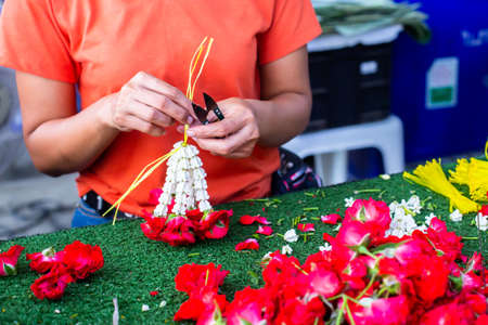 Asian woman staff is stringing flower garlands in flower shop at Bangkok flower market, Thailand.